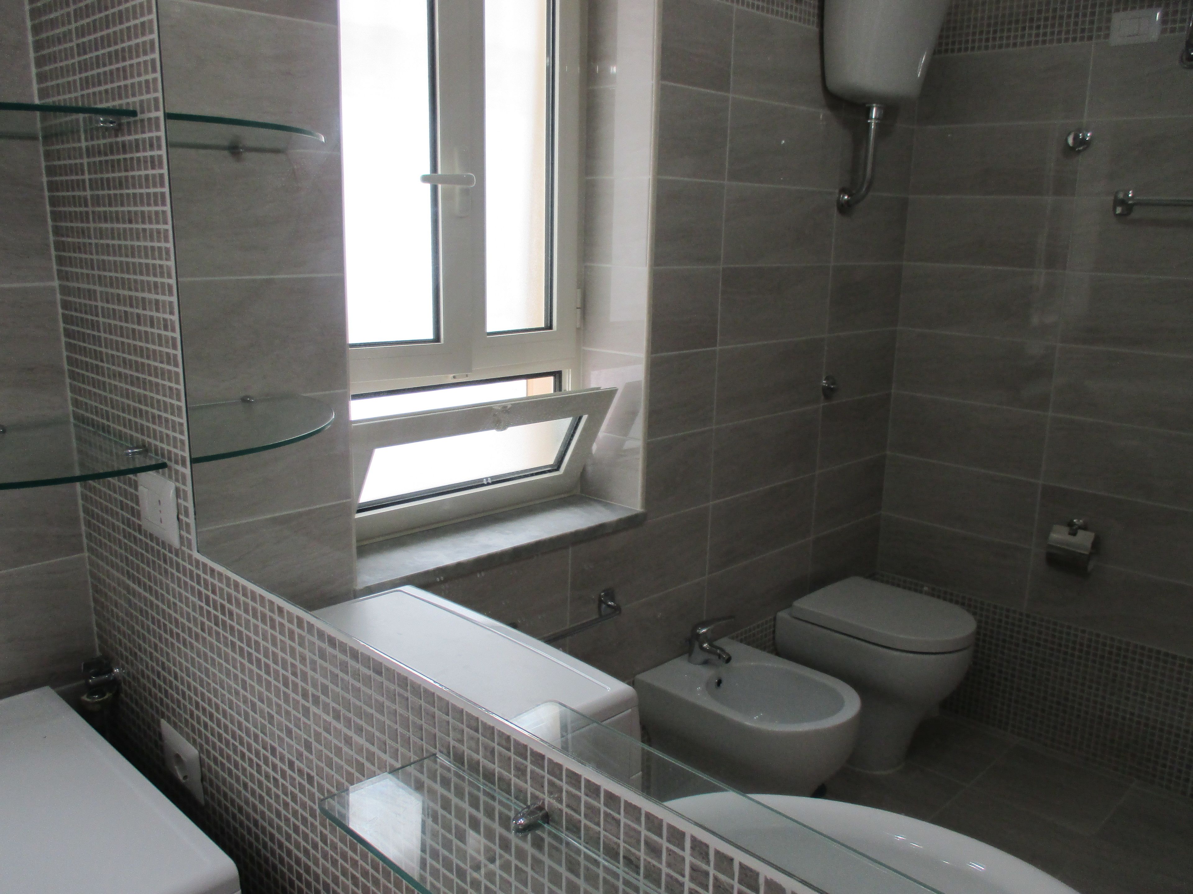 Un baño con inodoro, bidé y repisas de vidrio.