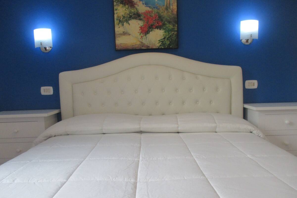 A bed with a tufted headboard in a room with blue walls and two wall-mounted light fixtures.
