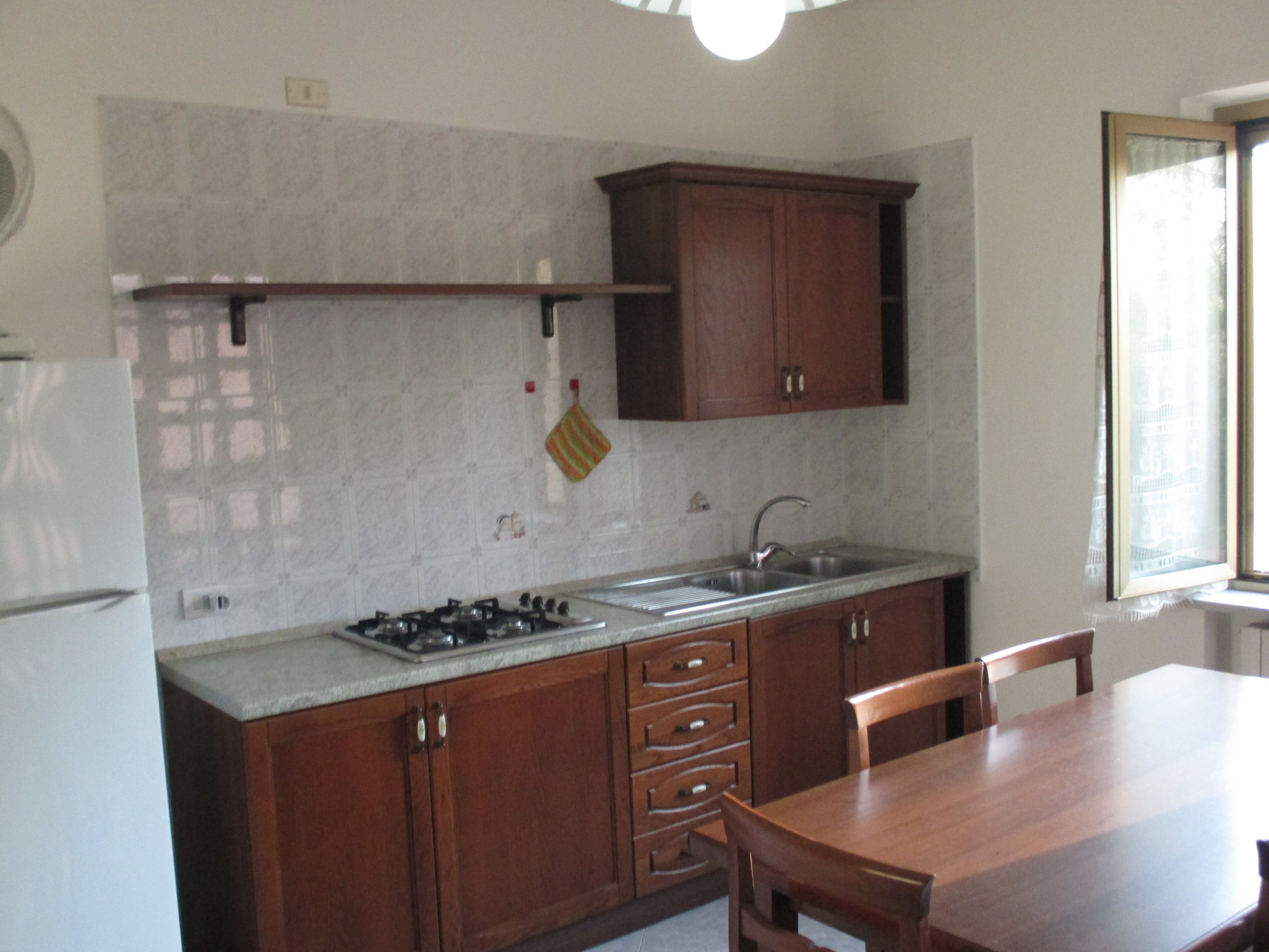 Una cocina con armarios de madera, una estufa a gas, un lavamanos y una mesa de comedor con sillas.