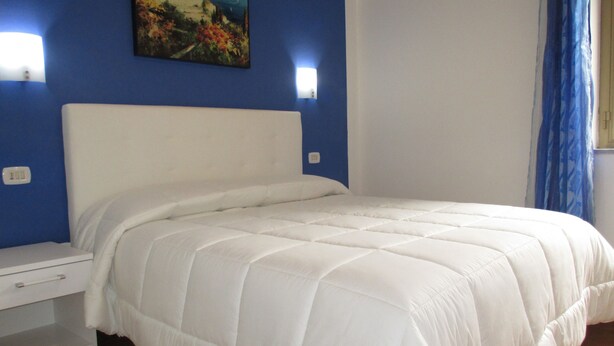 A bedroom with a white bed, blue walls, and a painting above the bed. - Casa Vacanze Donna Antonia (Centola)