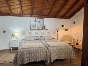 Un dormitorio con techo de madera, una cama con ropa de cama estampada, una mesita de noche con una lámpara y una silla.