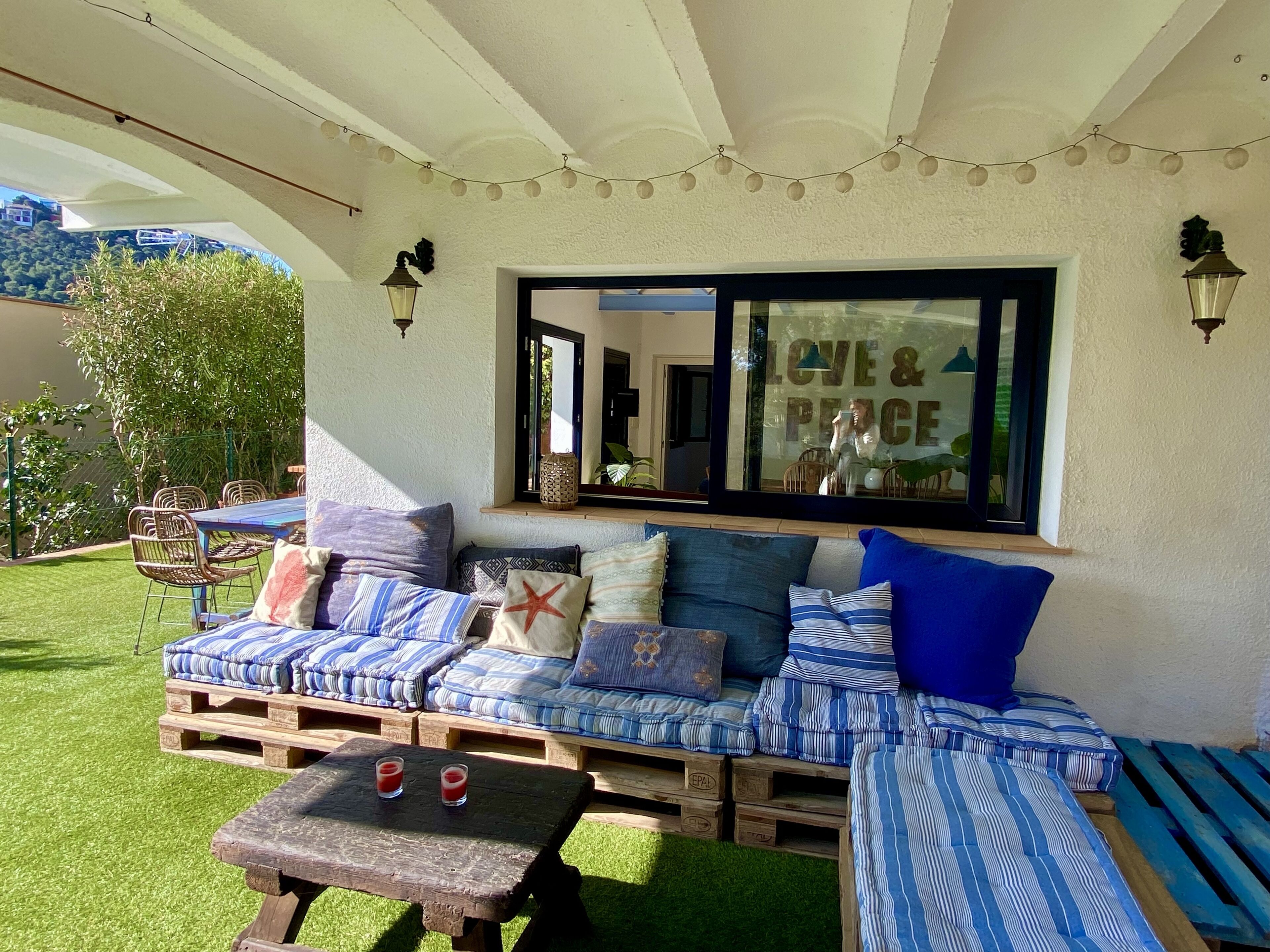 Un espace extérieur accueillant avec un banc en bois et un canapé confortable, une petite table avec des boissons et un panneau mural sur lequel on peut lire « AMOUR ET PAIX ».