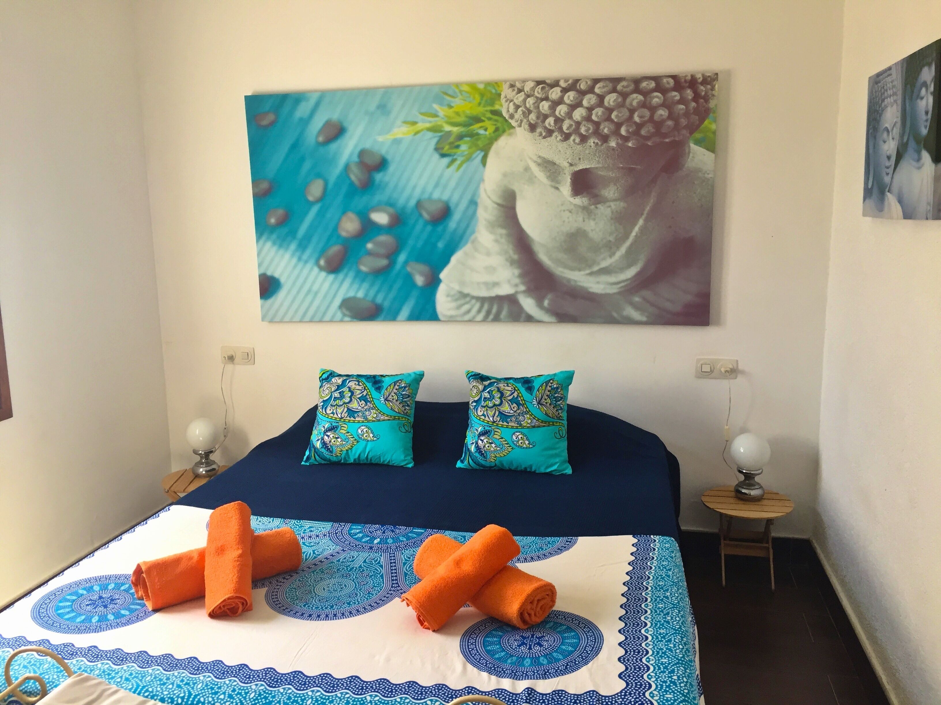 A bed with two decorative pillows, a blue and white patterned bedspread, and two rolled towels.