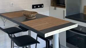 Moderni keittiö, jossa on puinen seinä, pyöreä kello, riippuvalaisimet, musta pöytä ja mustat tuolit.