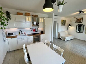 Une cuisine moderne avec des meubles blancs, un four à micro-ondes et un coin repas comprenant une table et des chaises blanches.