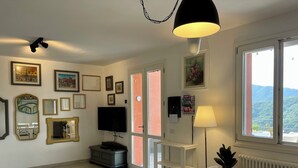 Ein Zimmer mit Fernseher, weißen Möbeln, einer Lampe und gerahmten Bildern an der Wand.