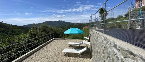 A rooftop terrace with a gravel floor, two lounge chairs, and a blue umbrella.