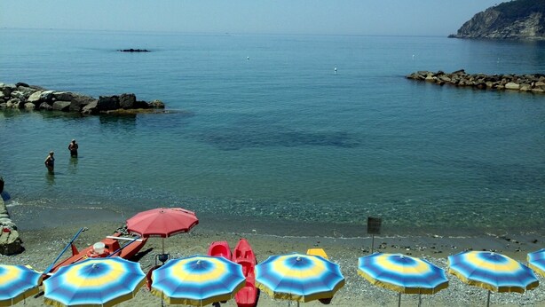Ein Strand mit klarem Wasser, felsigem Ufer und mehreren Sonnenschirmen.