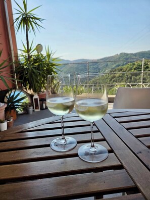 Two glasses of white wine on a wooden table with a view of green hills in the background. - Magic Littorno.Hills, sea, nature, hiking and swimming-pool (Littorno)