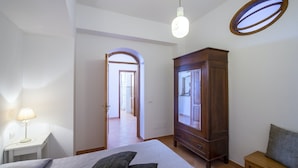 A bedroom with a bed, a wardrobe, a desk with a lamp, and a window with a view.