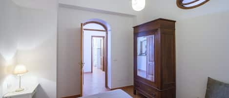 A bedroom with a bed, a wardrobe, a desk with a lamp, and a window with a view.