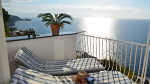 A balcony with a view of the sea, a potted plant, and a striped sofa with a hat and book.