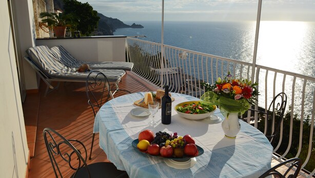 A balcony with a table set for a meal, overlooking a coastal view.