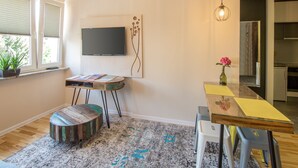 A modern living room with a flat-screen TV, a coffee table, a dining table, and a kitchen area visible through an open door. - Locum Magdalena Wroclaw Market (Wroclaw)