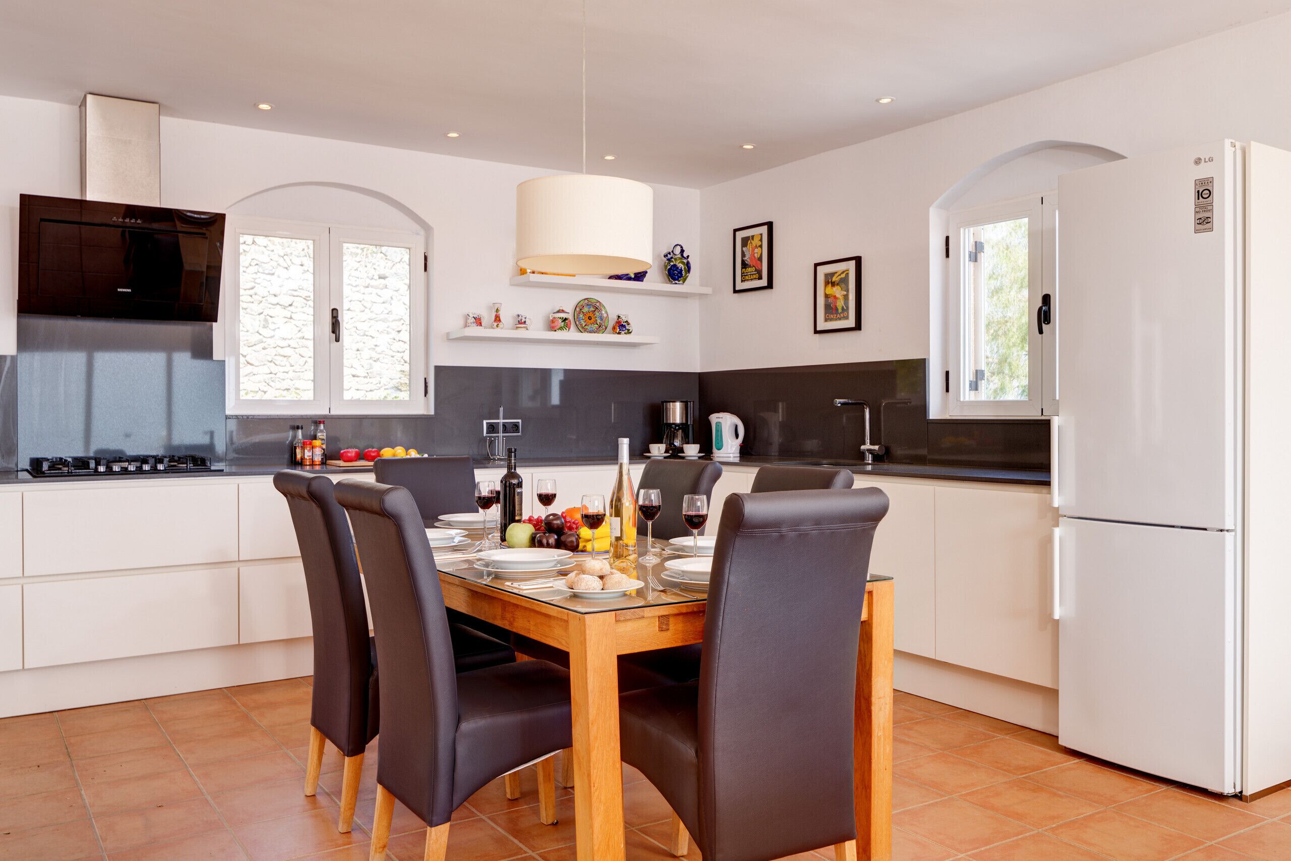 A modern kitchen with white cabinetry, a dining table set for four, and a built-in oven.