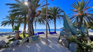 A beach scene with palm trees, a flag, and a statue. - Lovely 3 bedroom villa with private pool and lovely views (Almuñecar)
