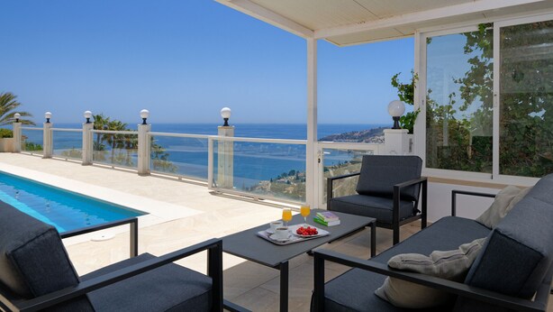 A balcony with a pool, seating, and a table with breakfast items. - Lovely 3 bedroom villa with private pool and lovely views (Almuñecar)