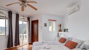A bedroom with a bed, curtains, an air conditioning unit, a ceiling fan, and a view through the door. - Lovely 3 bedroom villa with private pool and lovely views (Almuñecar)