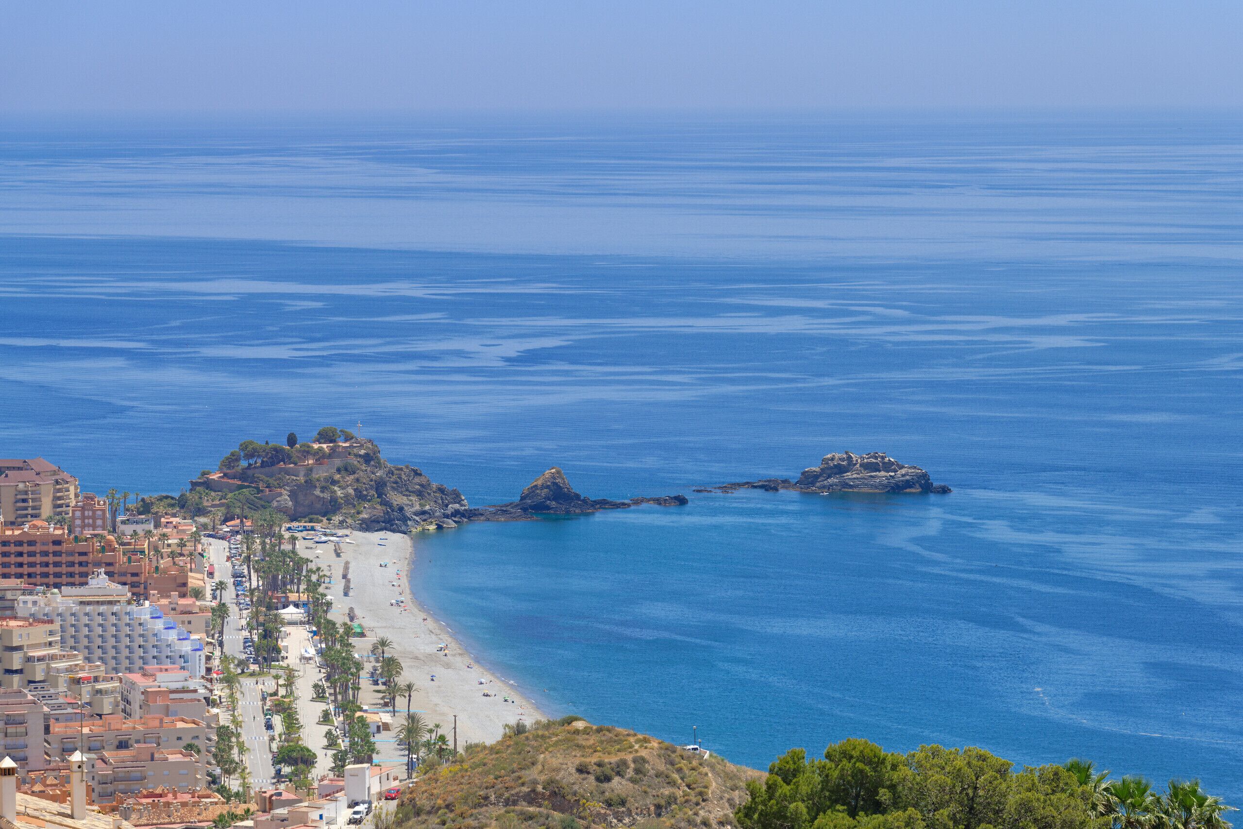 A coastal cityscape with a beach, rocky outcrops, and buildings along the shore.