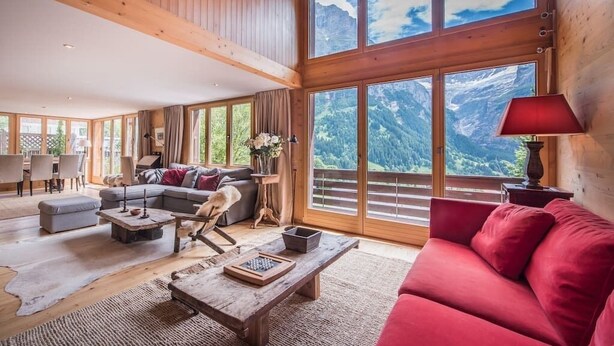 A spacious living room with a large window offering a mountain view, a red sofa, a wooden coffee table, and a dog. - Cozy free standing Chalet with garden and amazing mountain views (Grindelwald)