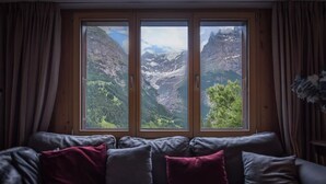 A room with a sofa facing a large window with a mountain view. - Cozy free standing Chalet with garden and amazing mountain views (Grindelwald)
