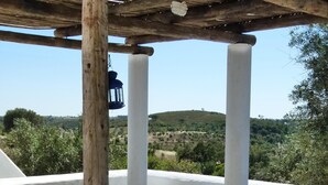 Une terrasse extérieure avec une table et des bancs en bois, entourée de murs blancs et d’un sol en pierre.