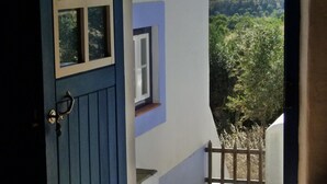 Une porte bleue qui donne sur un balcon agrémenté d’un escalier en pierre et offrant une vue sur la verdure.