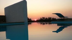 Un bâtiment moderne, doté d’un toit incurvé, situé près d’une étendue d’eau paisible, au moment du coucher du soleil.