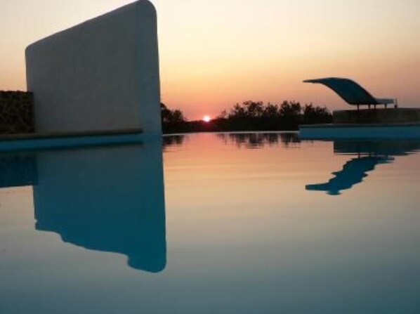 A modern building with a curved roof near a calm body of water during sunset.
