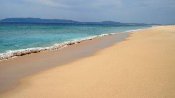 Une plage avec une eau d’un bleu limpide et une vaste étendue de sable.