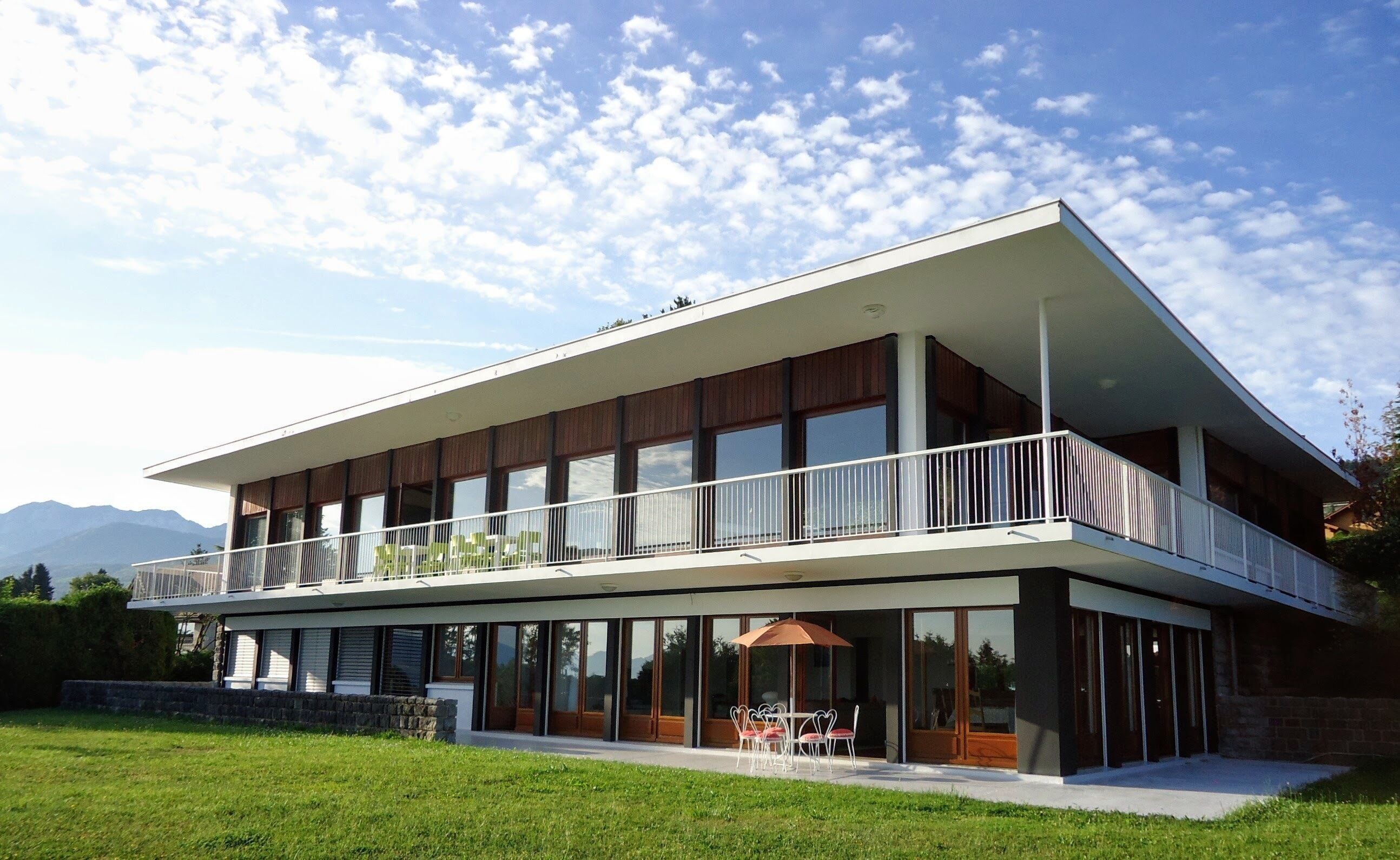 Ein modernes, zweistöckiges Haus mit Balkon, großen Fenstern und einem Rasen.