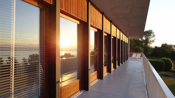 Un edificio moderno con grandes ventanales y un balcón con vistas a un cuerpo de agua.