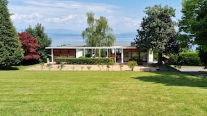 Una casa moderna con un amplio jardín, vista al agua y cielo despejado.