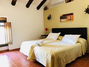 A double bed with white linens and a headboard, a small bedside table with a lamp, and a window with a wooden frame. - Holiday cottage for 10 people near Antequera (Malaga) (Villanueva de Algaidas)