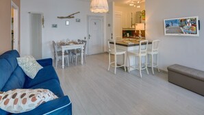 Un salon avec un canapé bleu, un coin repas avec une table et des chaises, une cuisine avec un comptoir et des appareils électroménagers, et un banc.