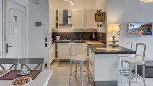 Une cuisine compacte avec des meubles blancs, un îlot central doté de tabourets, une table à manger avec des chaises et un petit coin salon avec un canapé.