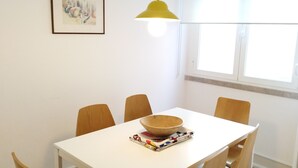 En matplats med ett vitt bord, fyra trästolar, en skål och en färgglad bordsduk.