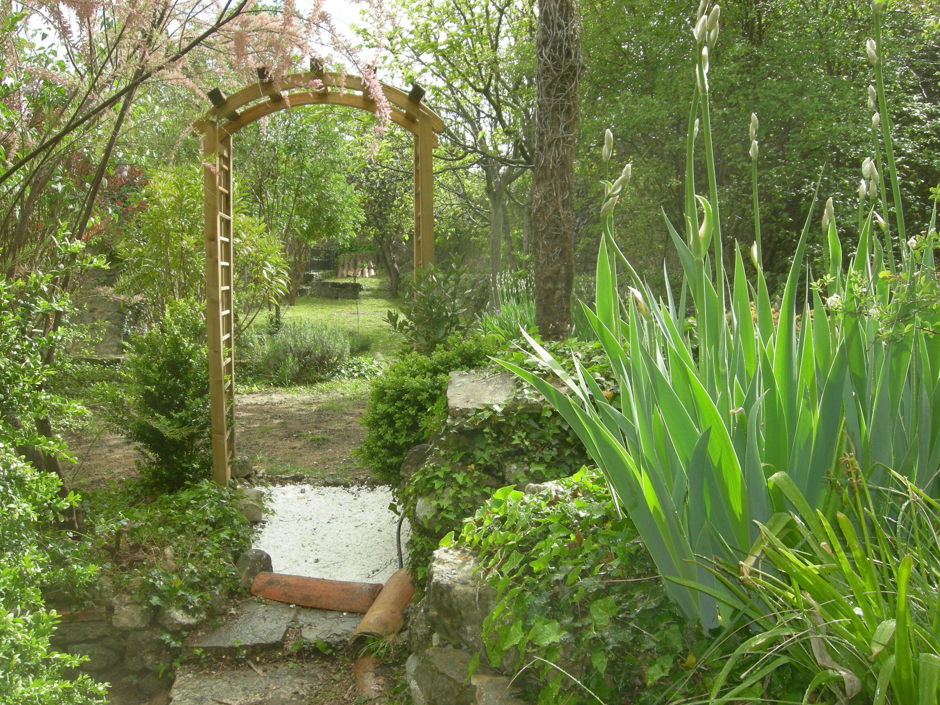 Un sendero en un jardín que conduce a un arco de madera rodeado de abundante vegetación y plantas.