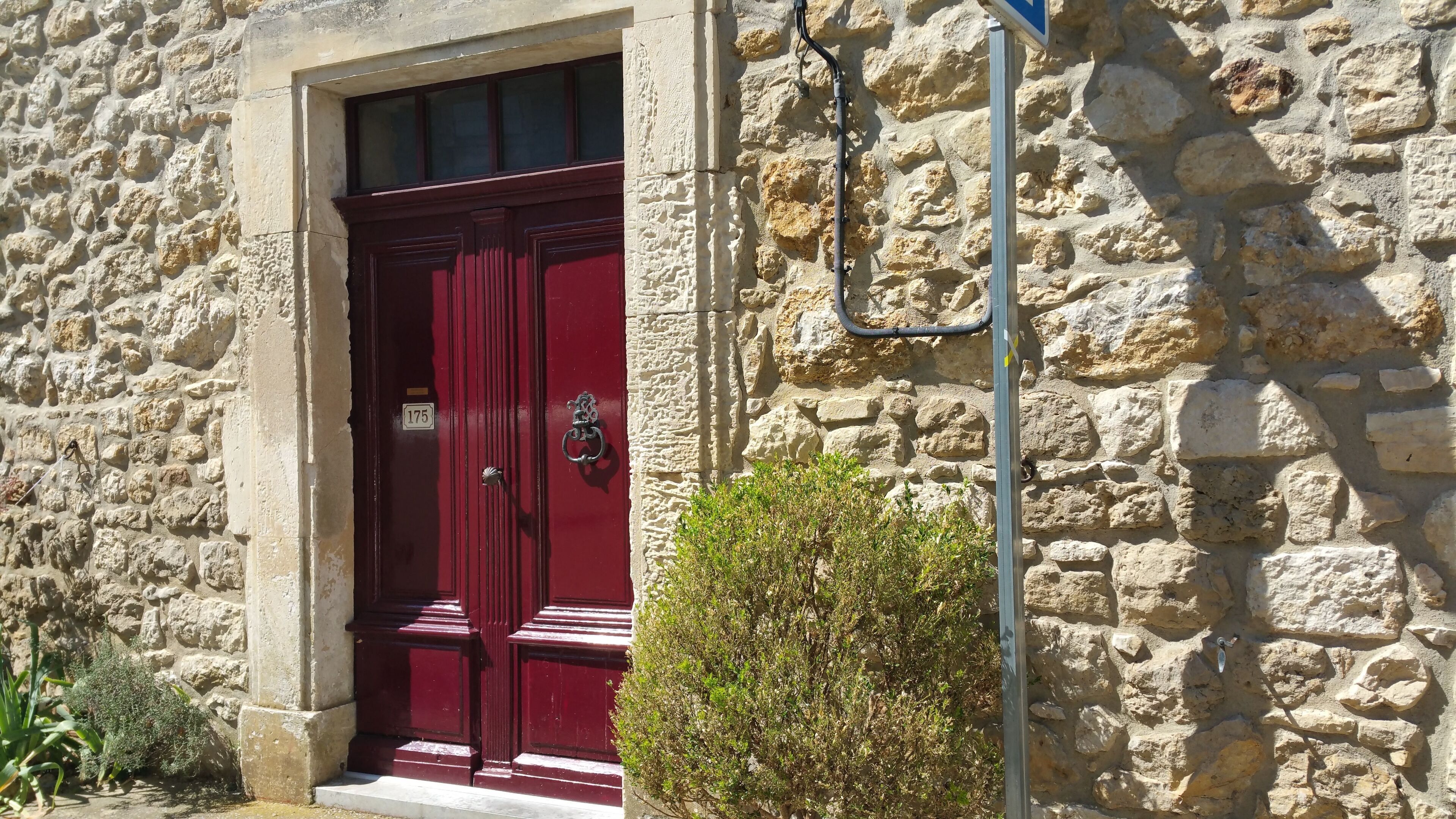 A stone building with a red door, a small bush in front, and a utility pole with a cable.
