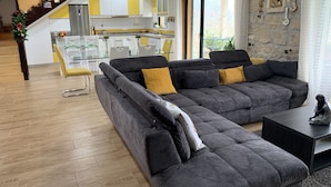 Una sala moderna con un sofá seccional gris, una mesita negra y una escalera que lleva a una cocina con gabinetes amarillos.