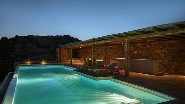 Una piscina con sillas de descanso y un muro de piedra de fondo.