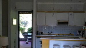 Una cocina compacta con armarios blancos, una isla central con taburetes y un acceso al exterior.