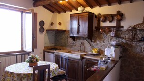 A kitchen with stone walls, wooden cabinets, and a dining table with a floral tablecloth. - Beautiful stone house with garden and private pool. (Sovicille - Siena)