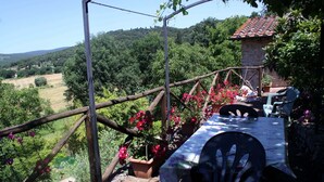 A rustic outdoor seating area with a table and chairs, surrounded by potted plants and flowers, overlooking a lush valley. - Beautiful stone house with garden and private pool. (Sovicille - Siena)