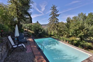 A rectangular swimming pool with a wooden deck, surrounded by lush greenery and trees. - Beautiful stone house with garden and private pool. (Sovicille - Siena)