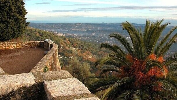 Un sentier de pierres qui mène à un belvédère offrant une vue panoramique sur une ville et des montagnes lointaines.