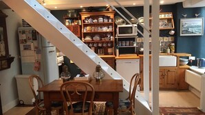 A kitchen with a white staircase, wooden cabinets, and a variety of kitchenware. - Charming Fisherman's Cottage in lovely fishing port close to Penzance (Newlyn)