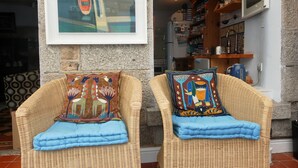 Two wicker chairs with colorful cushions, a stone wall, and a kitchen area with shelves and appliances. - Charming Fisherman's Cottage in lovely fishing port close to Penzance (Newlyn)