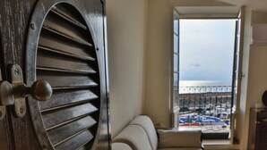 Ein Zimmer mit einem großen Fenster, einem Sofa und Blick auf einen Balkon mit Geländer.