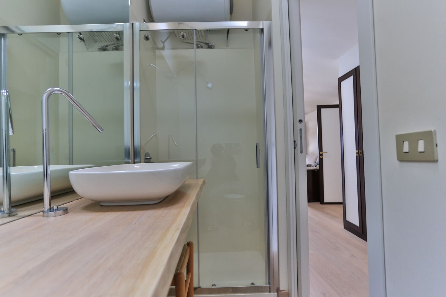 A modern bathroom with a glass shower enclosure, a white sink, and a wooden countertop.